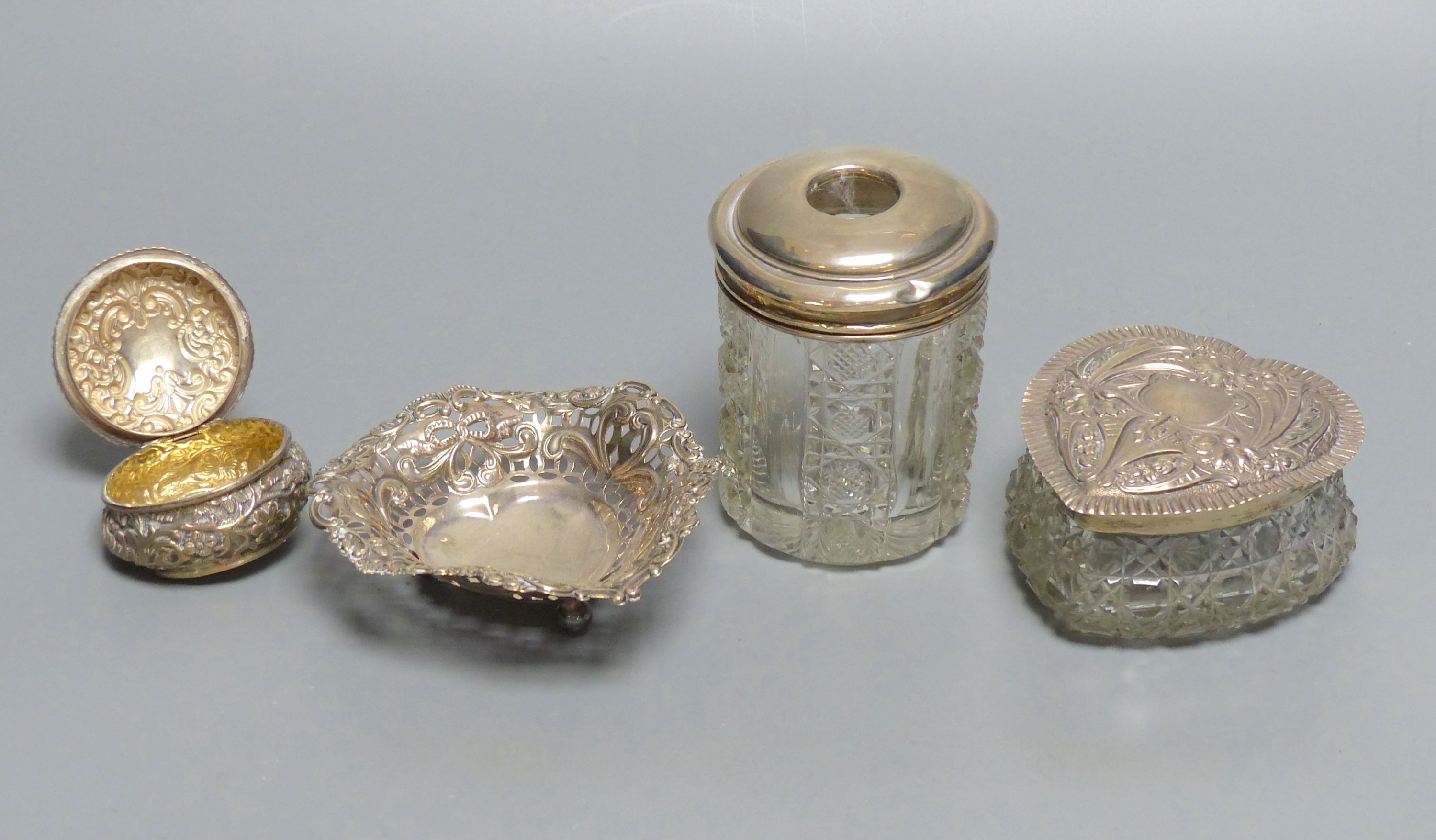 A heart-shaped cut glass box with repousse silver lid and three other dressing table items,